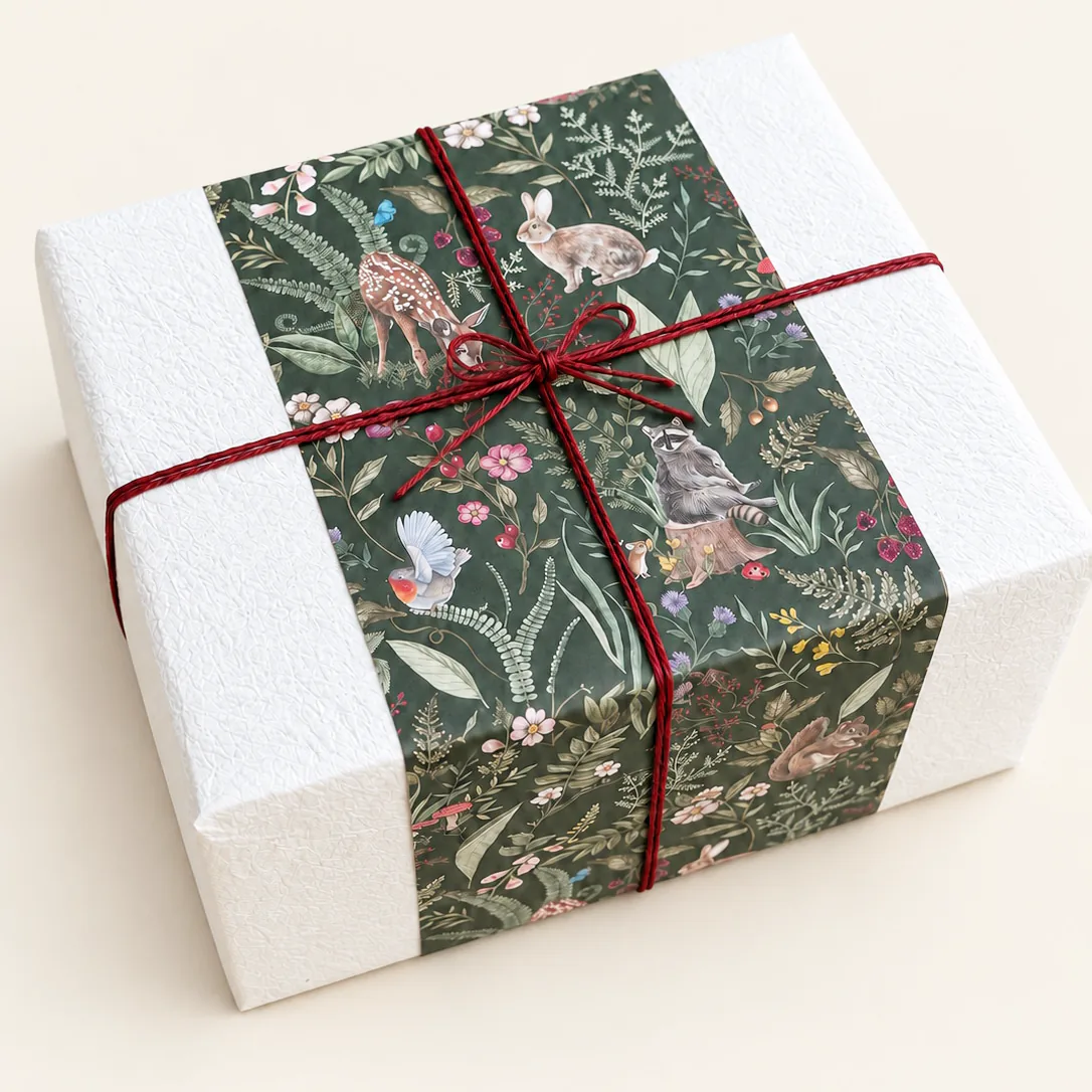 A white box banded with dark green botanical paper and tied with a deep red cord.